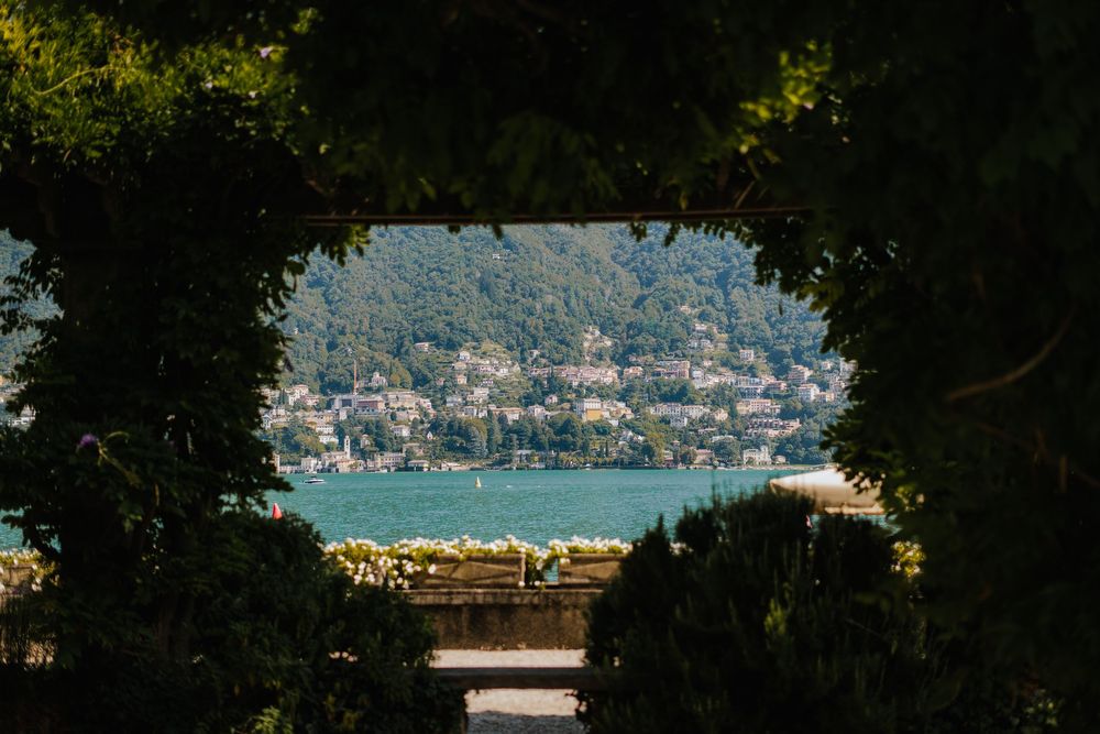 Panoramic vista of mountain lake surrounded by forest with small village nestled along the shoreline under blue skies.