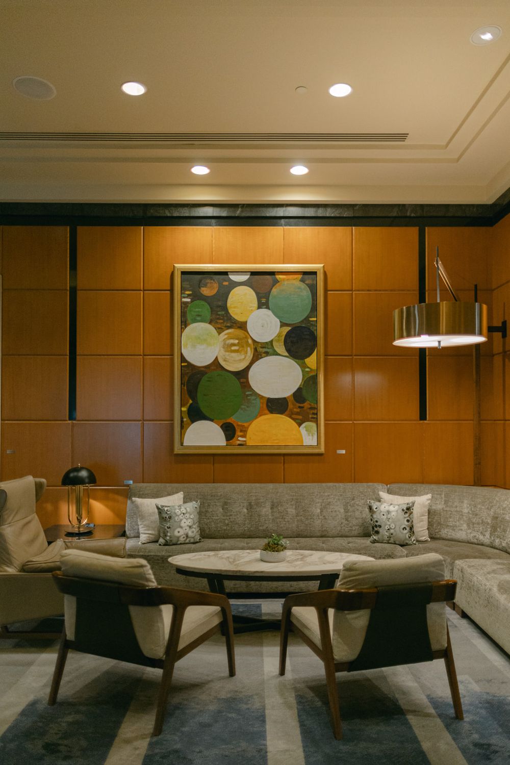 Modern hotel lounge area with luxurious grey sectional seating and wood paneled walls in warm lighting.