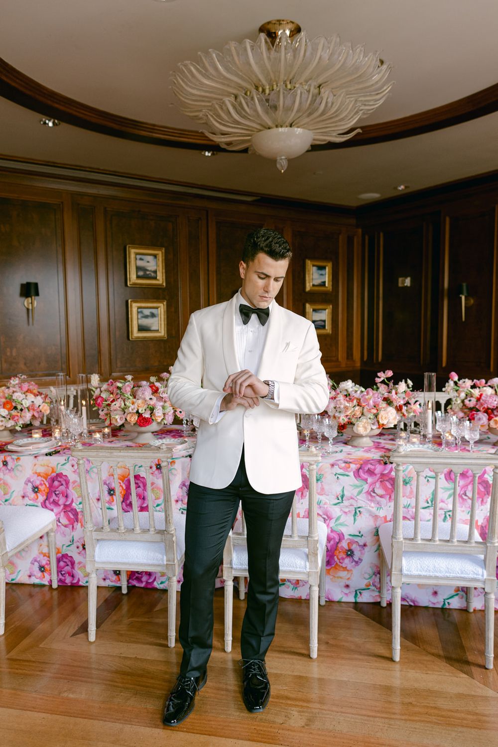 Elegant wedding reception setup with floral decor and chandelier in wood-paneled room.