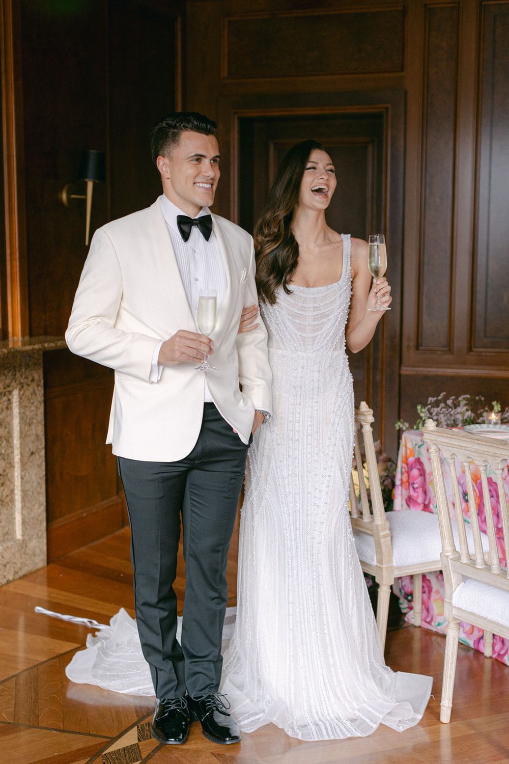 Elegant couple shares champagne and laughter at a wedding celebration in formalwear.