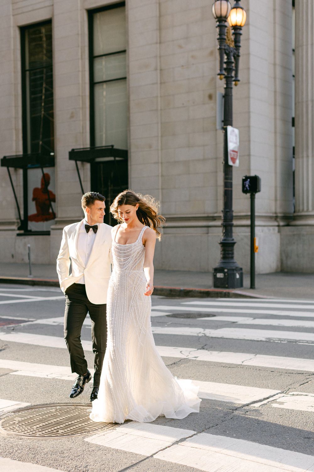 Bride and groom walking together on city street near vintage lamp post.