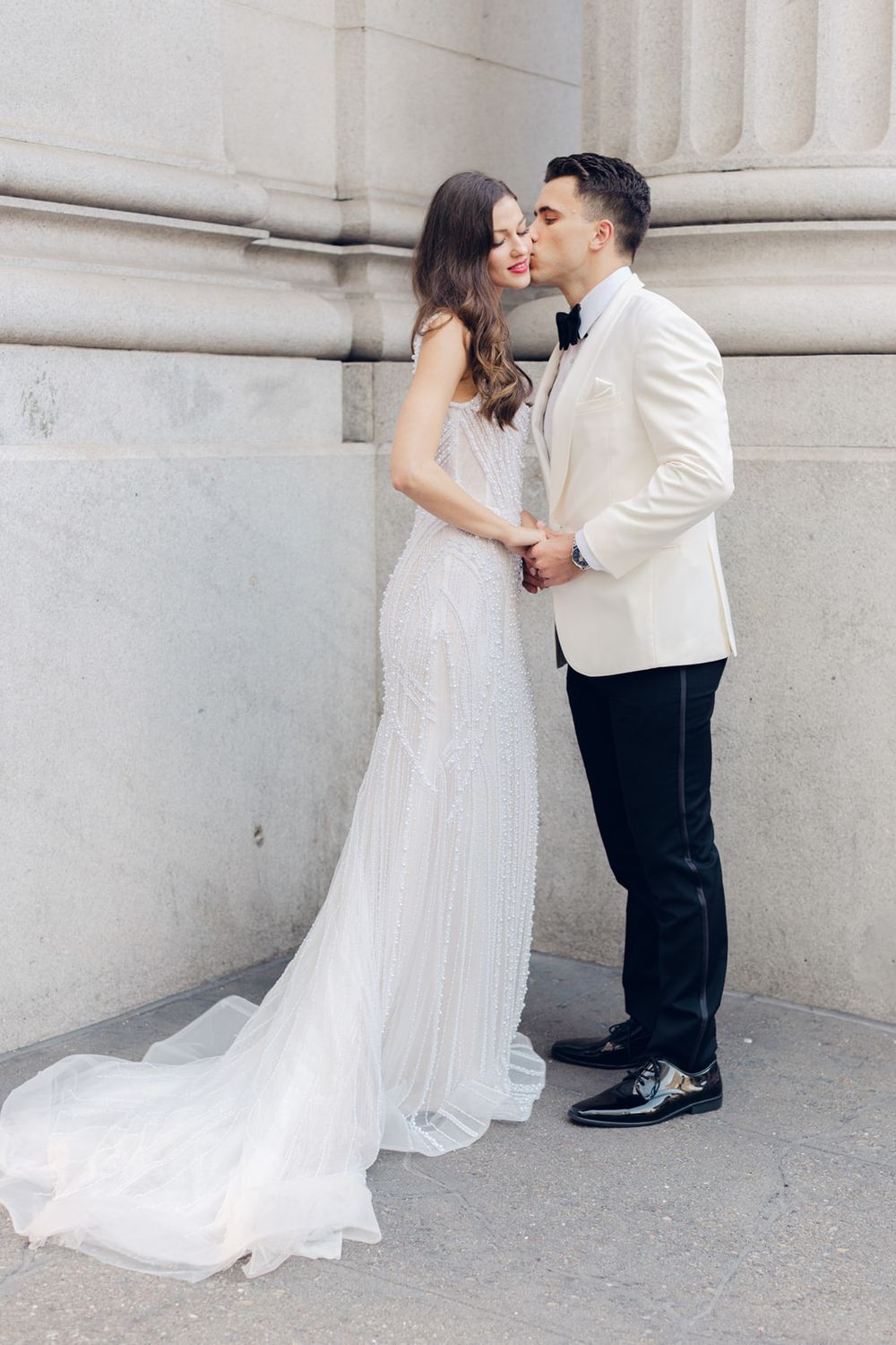 A romantic moment between newlyweds against a classic white stone building facade.