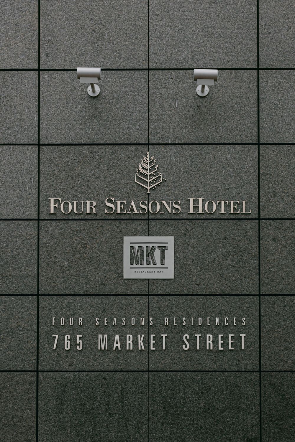 Sign for Four Seasons Hotel and Four Seasons Residences at 765 Market Street mounted on grey stone wall.