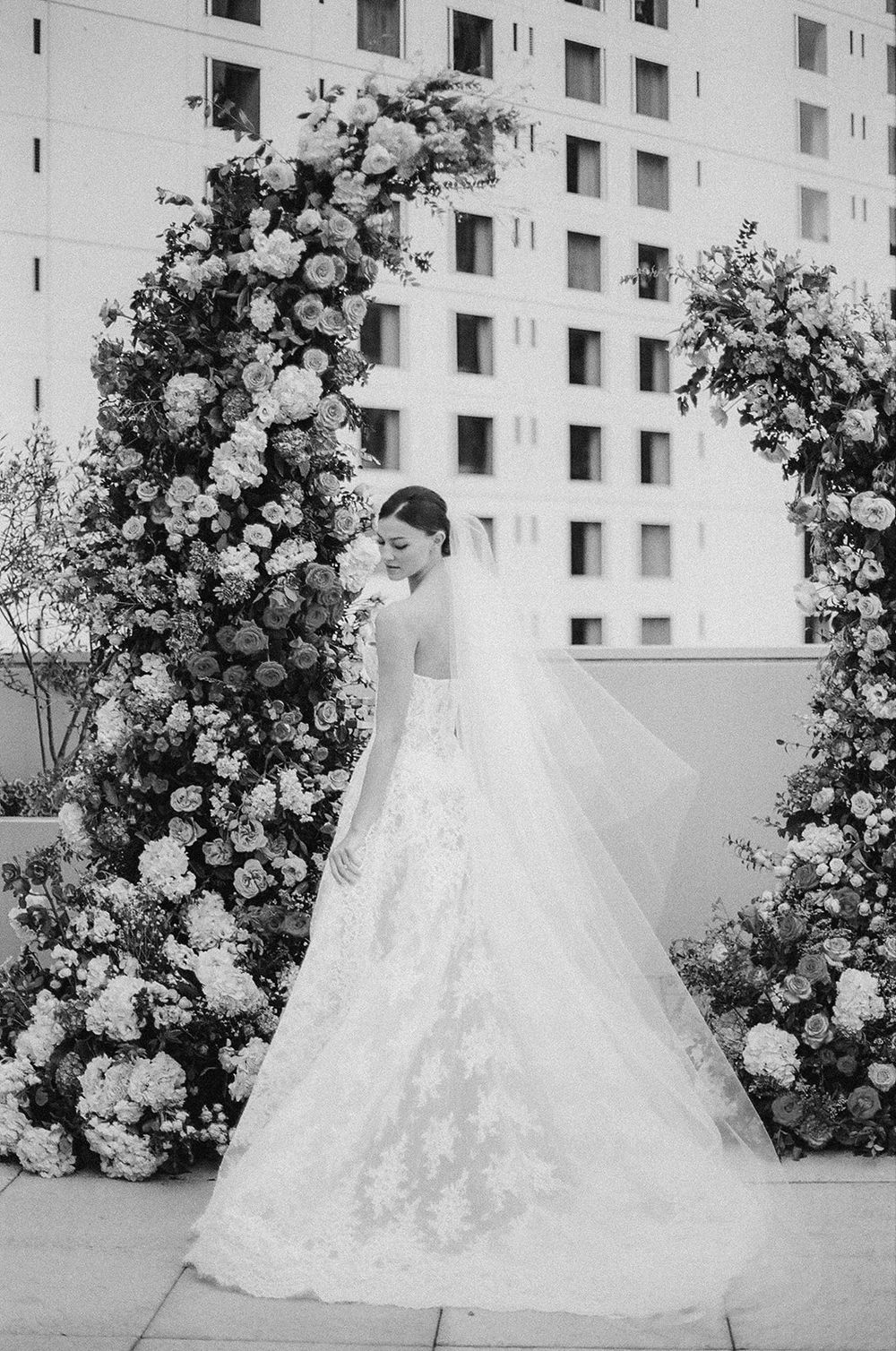 A series of black and white wedding photos showing a bride in a flowing lace gown against a floral backdrop.