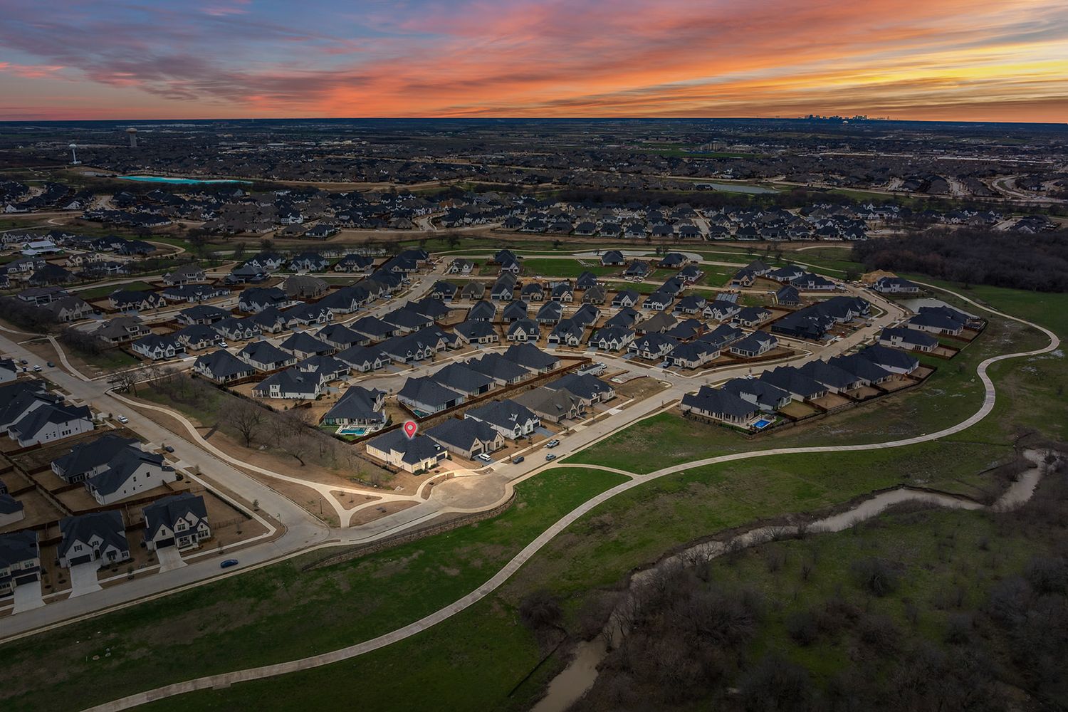 A suburban housing development at sunset with curved streets and residential homes viewed from an aerial perspective.