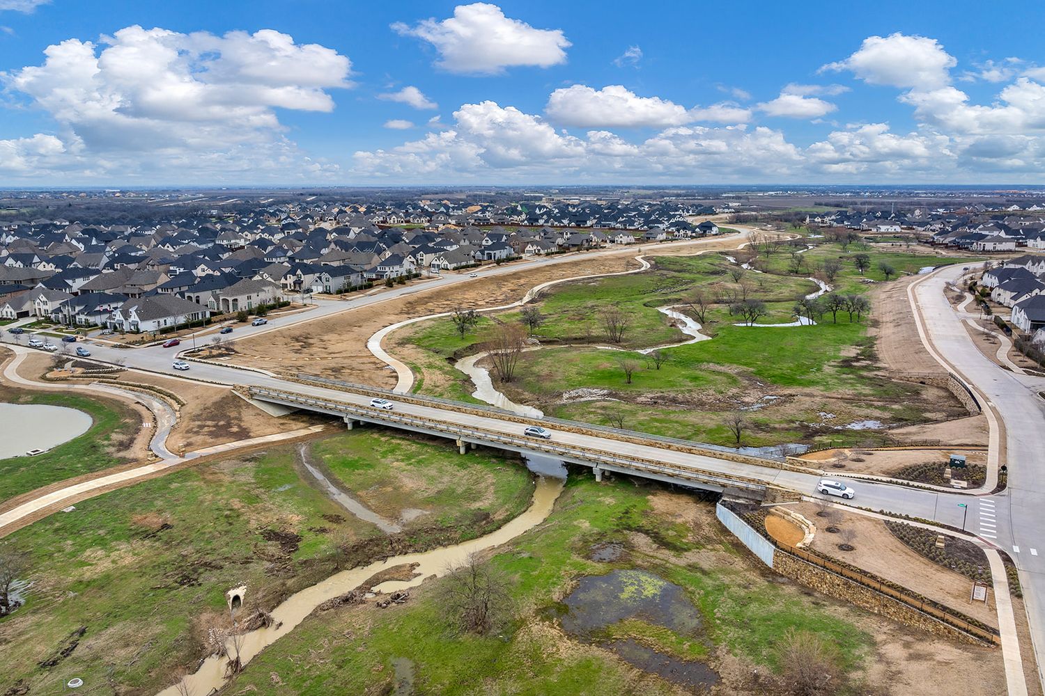 Aerial view of highway interchange construction with curved roads and green fields under blue skies with white clouds.