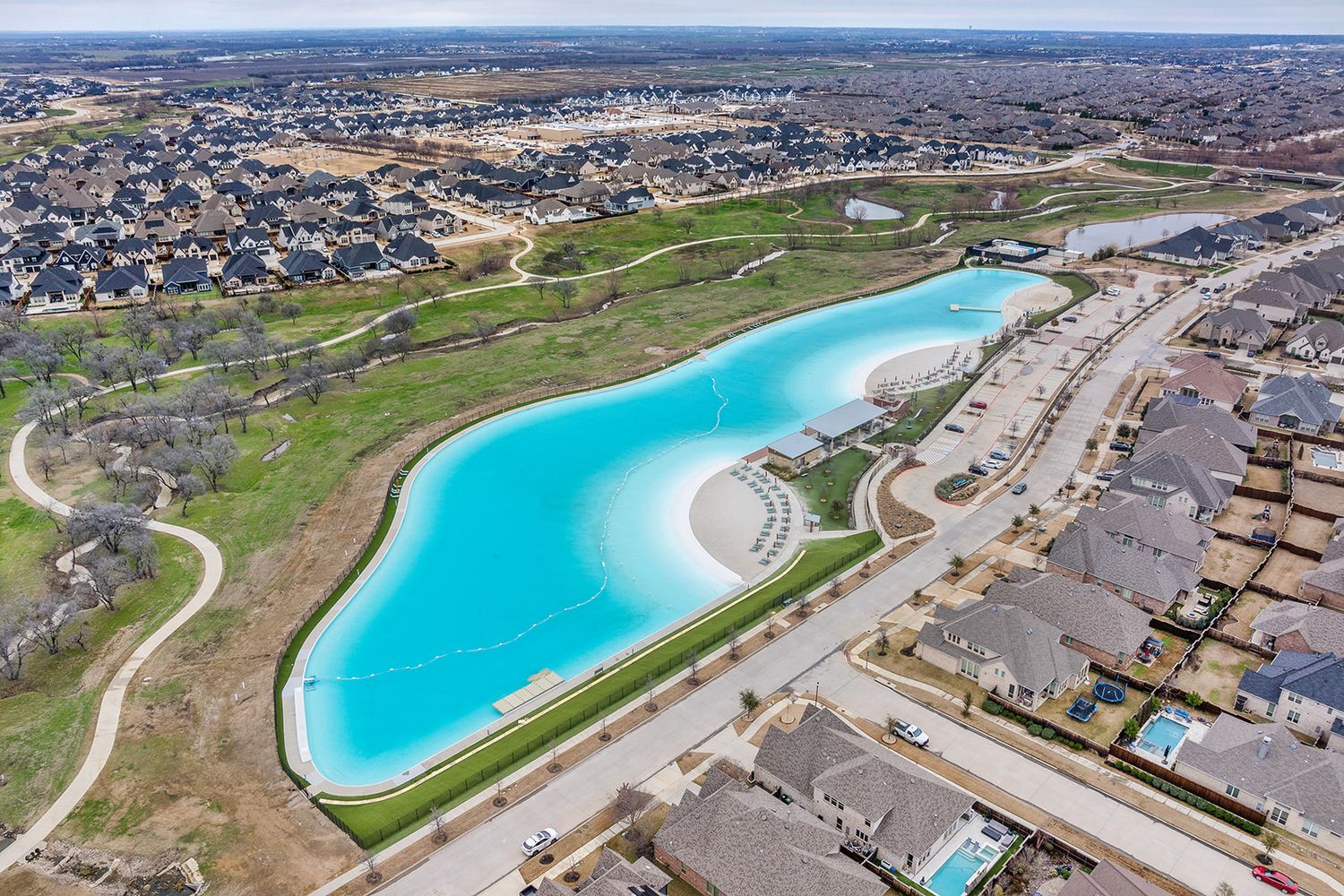 Aerial view of a bright turquoise lagoon surrounded by residential homes and green spaces in a suburban development.