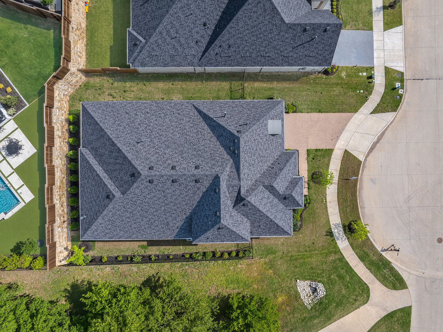 Aerial photo shows gray-roofed houses in a suburban neighborhood with green lawns and paved driveways.