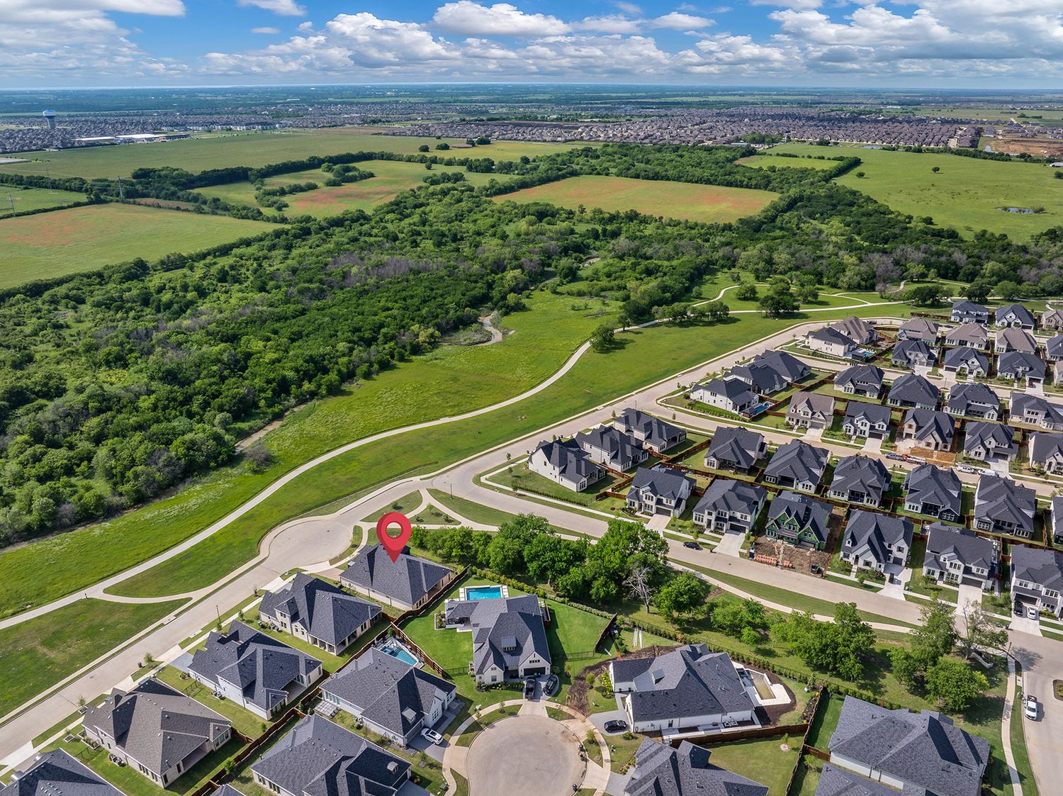 Aerial view of a suburban housing development next to green park space and rolling farmland under blue skies.