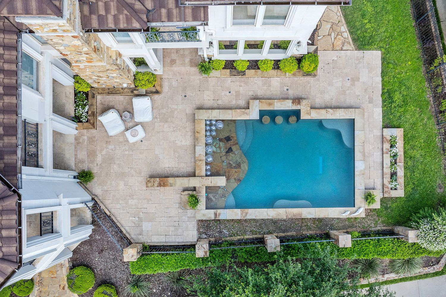 Aerial view showing multiple rectangular swimming pools surrounded by stone patios and landscaped yards in a residential area.