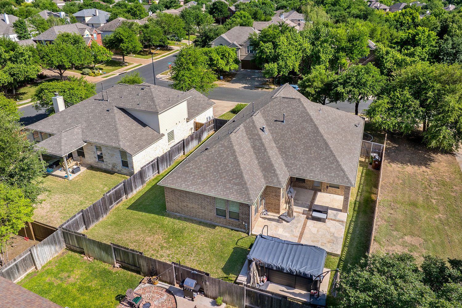 Aerial view of residential houses with green lawns and trees in a suburban neighborhood on a sunny day.
