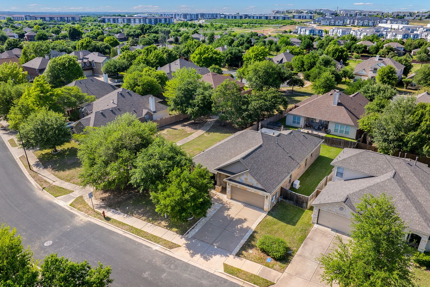 Aerial view of residential neighborhood with curved street, green trees, and suburban houses with neat lawns.
