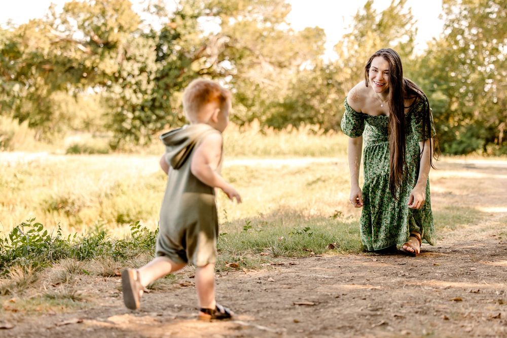 A joyful moment captured on a sunlit dirt path as a small child runs towards someone in a flowing green dress in nature at fort worth park