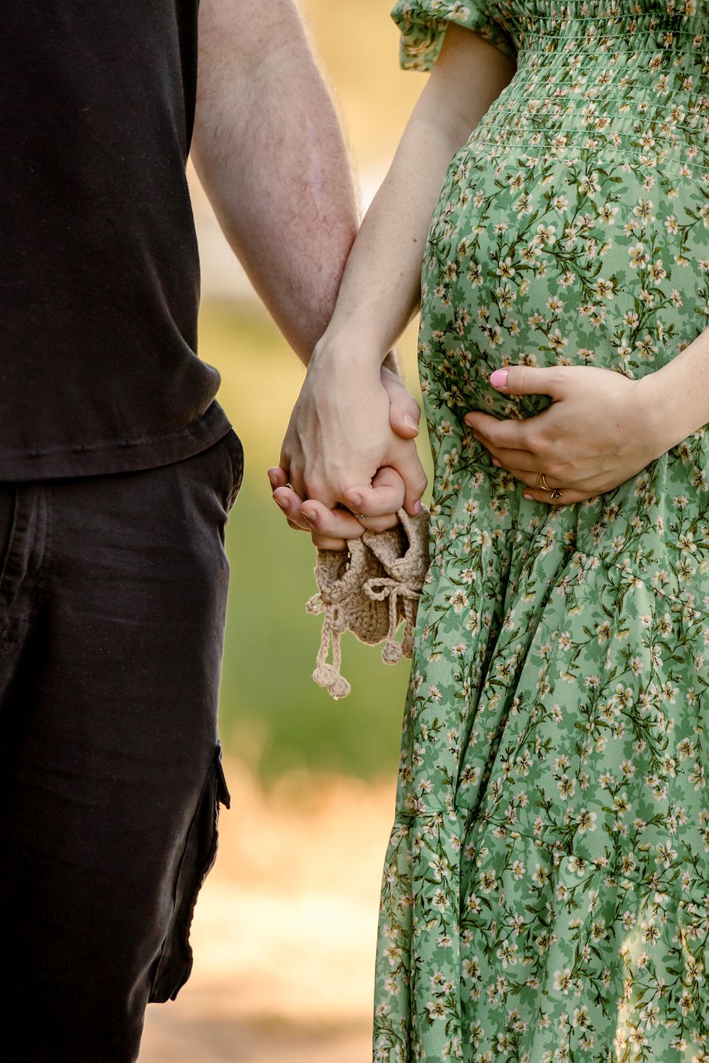 Close-up view of hands holding each other against a green floral dress and black clothing in soft outdoor lighting.