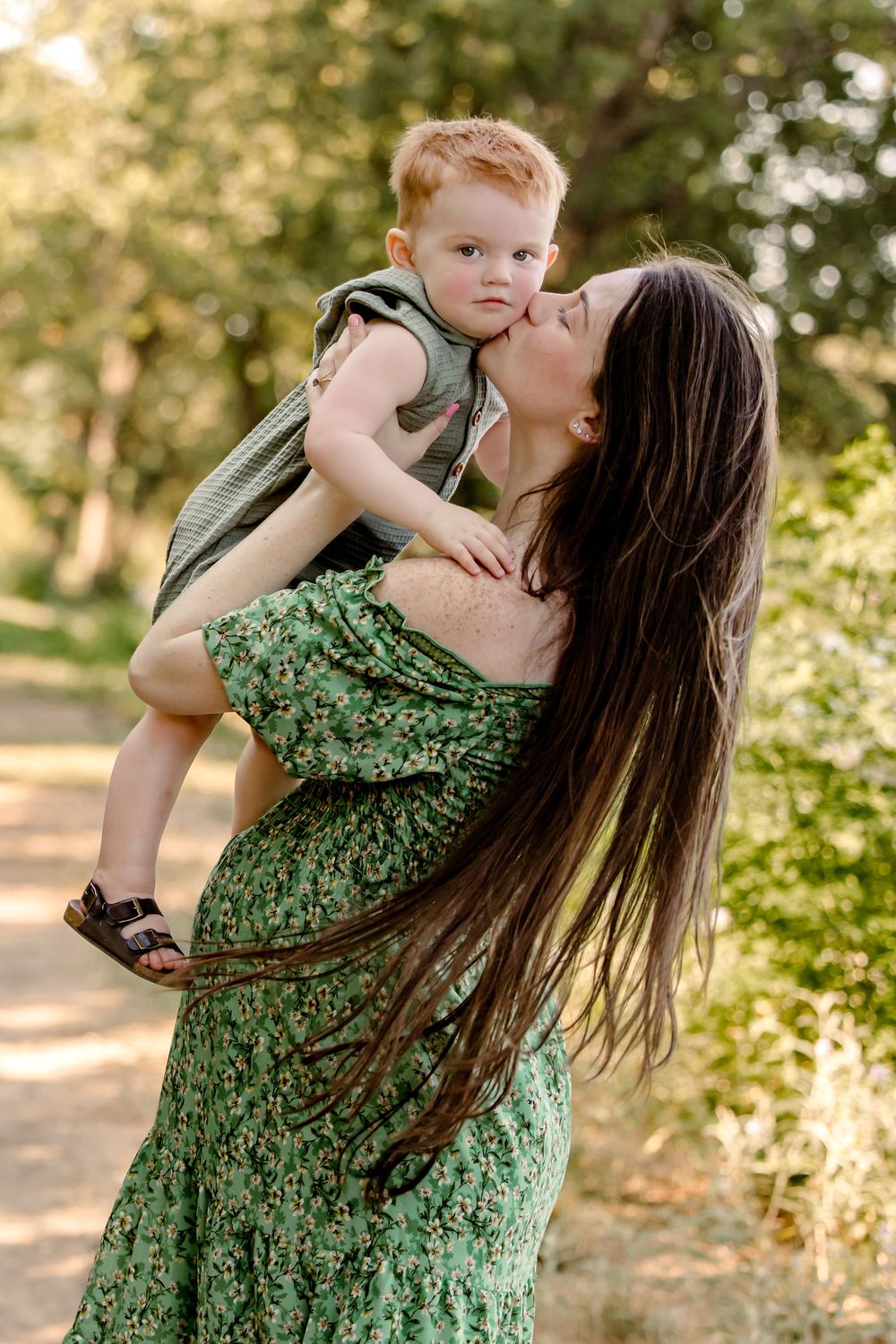 A parent in a green floral dress holds a small child outdoors at fort worth photo session
