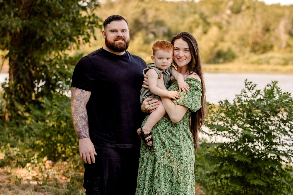 A couple embraces in a golden outdoor setting during sunset wearing black and green outfits surrounded by natural scenery in fort worth