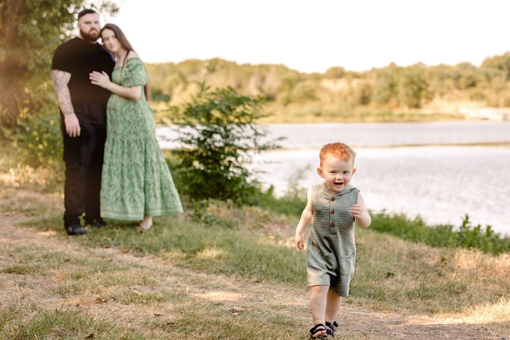 A family in coordinating brown and sage green outfits walks together along a scenic lakeside path at sunset in fort worth