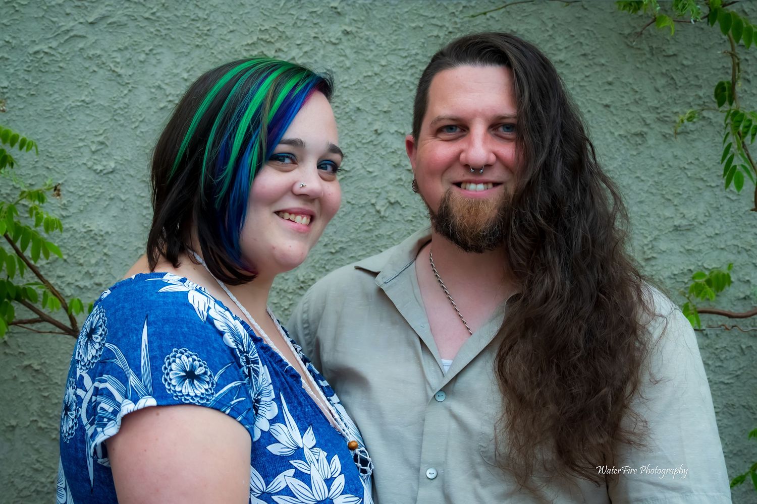 A couple poses together against a mint green wall with vines.