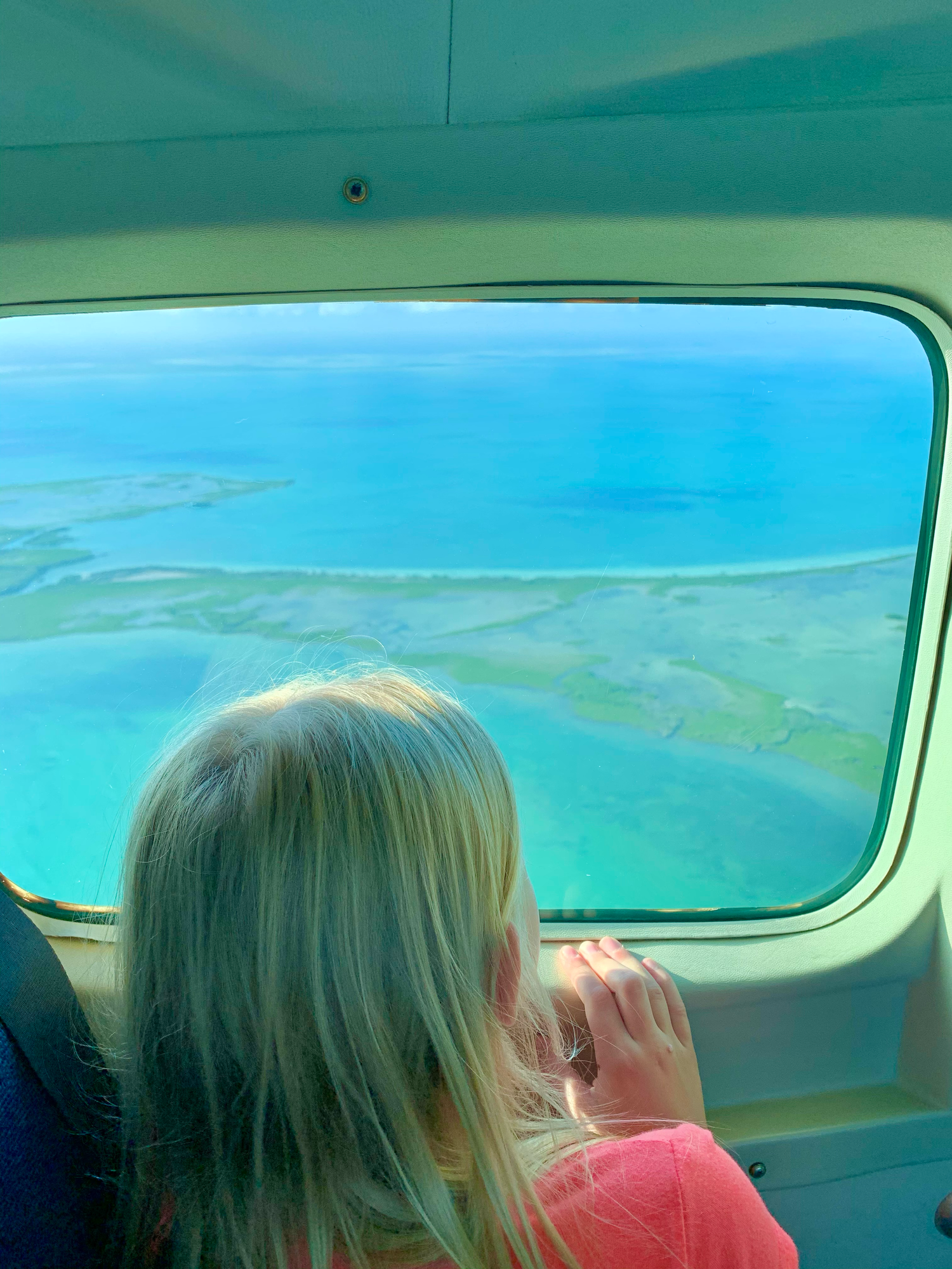 View through airplane window showing turquoise waters and coastal landscapes below.