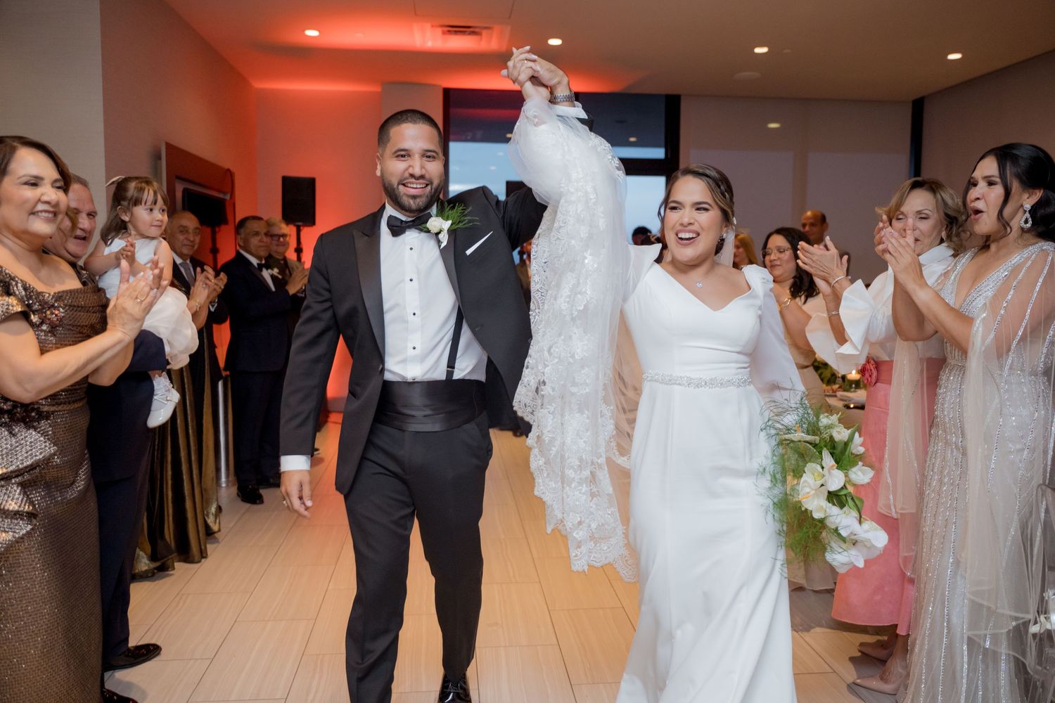 A couple makes their joyful entrance into a reception venue as wedding guests line up to celebrate their special moment.