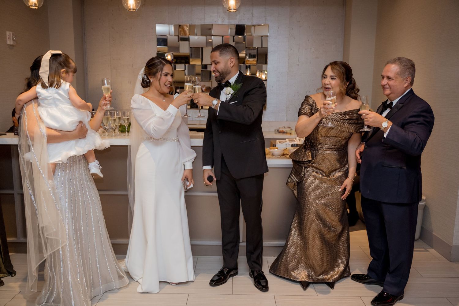 Wedding party members in formal attire celebrate together with drinks at an indoor reception.