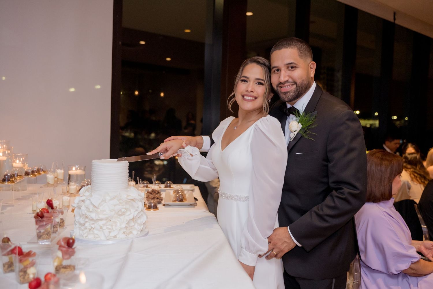 A bride and groom share a joyful moment while cutting their elegant white wedding cake at their reception.