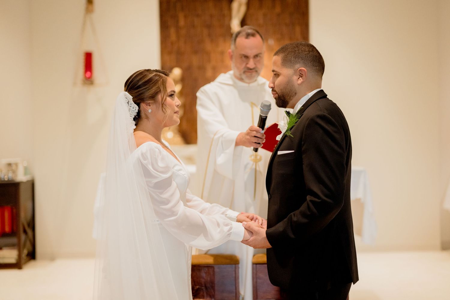 Wedding ceremony with bride in white gown and groom in black suit exchanging vows before an officiant at the altar.