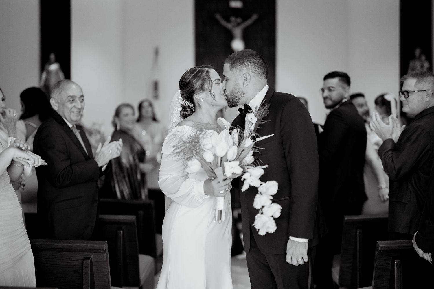 A romantic kiss shared between newlyweds during their wedding ceremony in a church with guests in attendance.