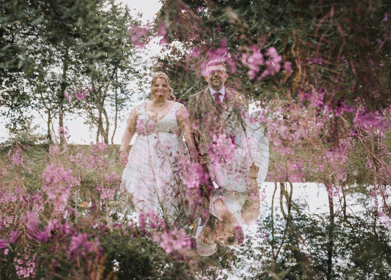 A couple walks hand in hand through a garden filled with vibrant pink flowers on their wedding day.