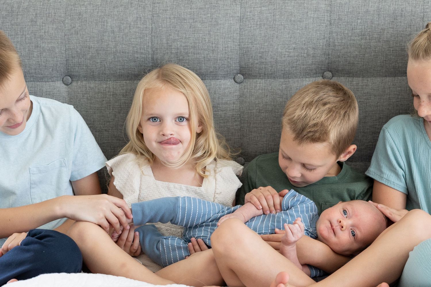 5 kids sitting on bed. one little girl licking her lips silly at the camera
