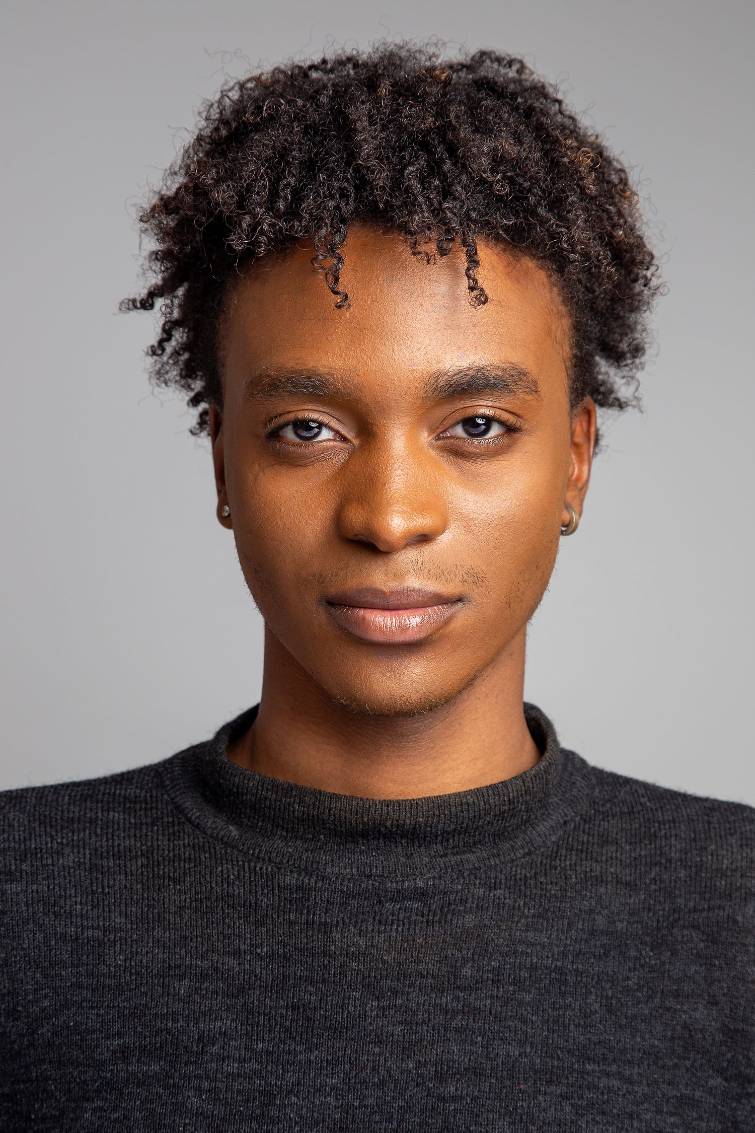 Professional studio portrait showing a contemplative pose wearing a black sleeveless top against a gray background.