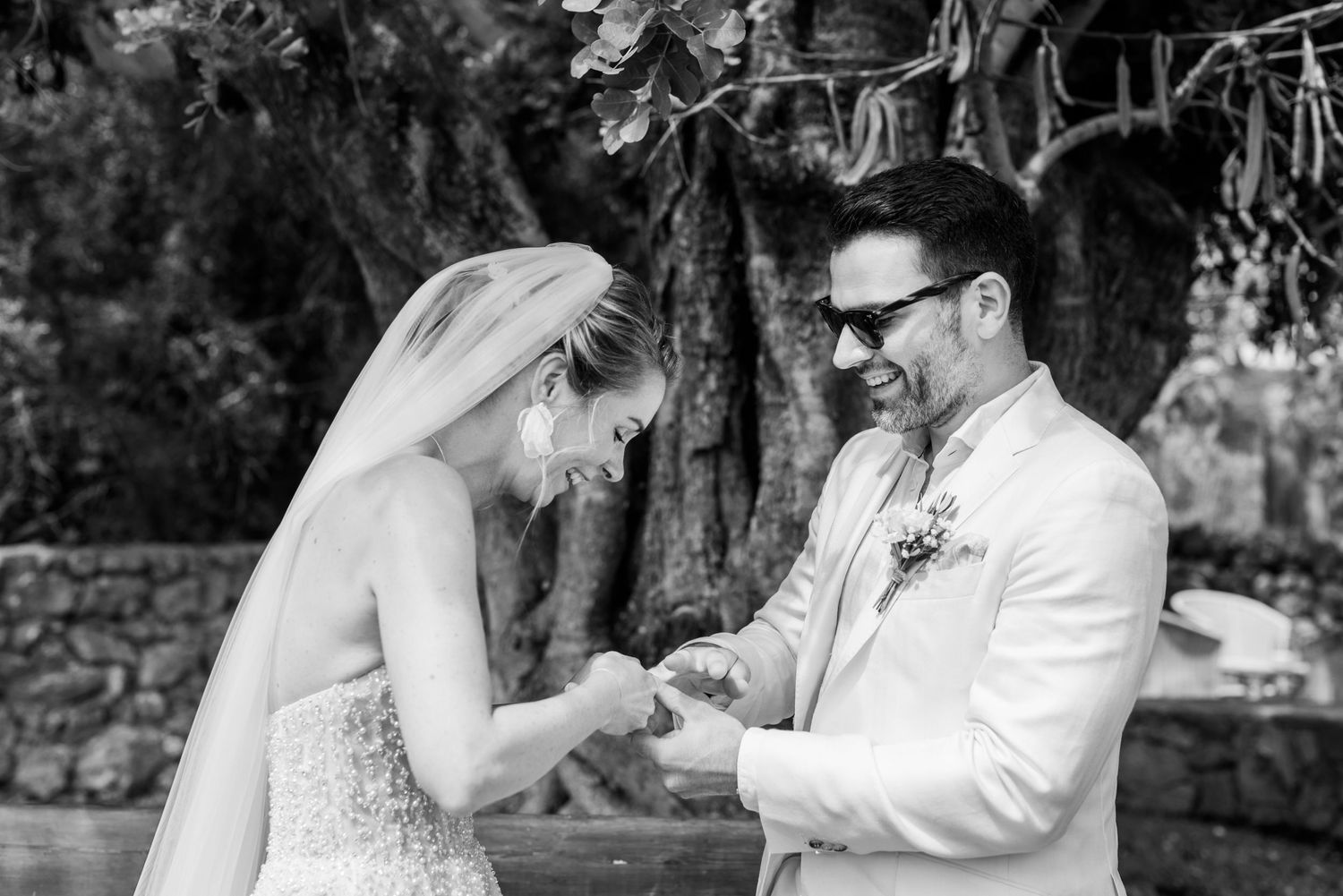 Das Hochzeitspaar teilt romantische Momente während einer Fotosession unter einem Baum auf einer sonnigen Wiese im Freien und tauscht Ringe.