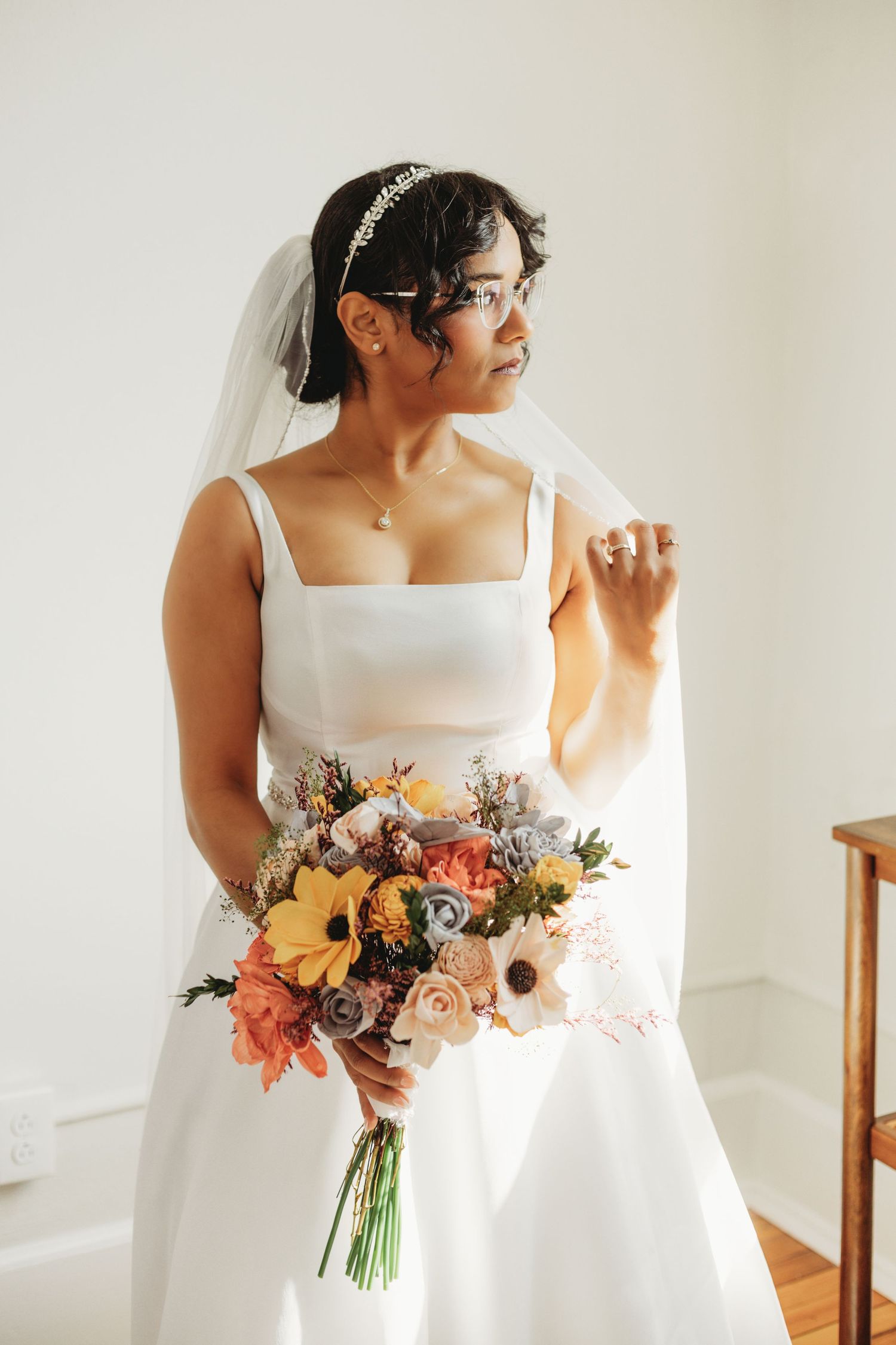 Wedding dress and colorful bouquet featuring orange and pink flowers against a white background.