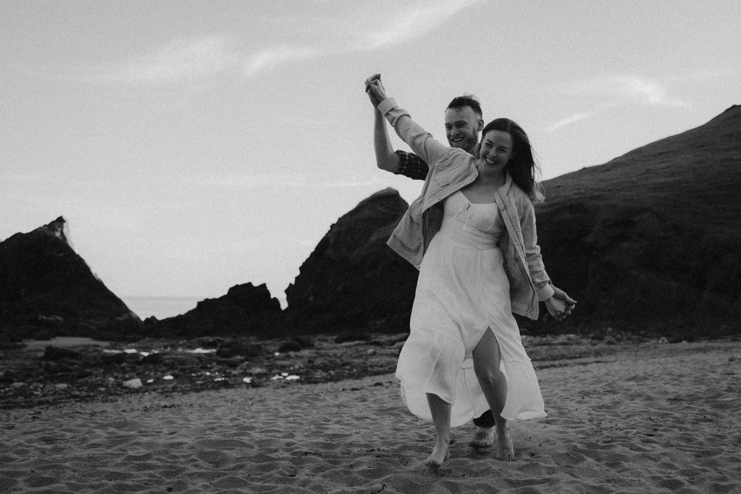 Two people walk along a misty beach at sunset as waves roll onto the shore.