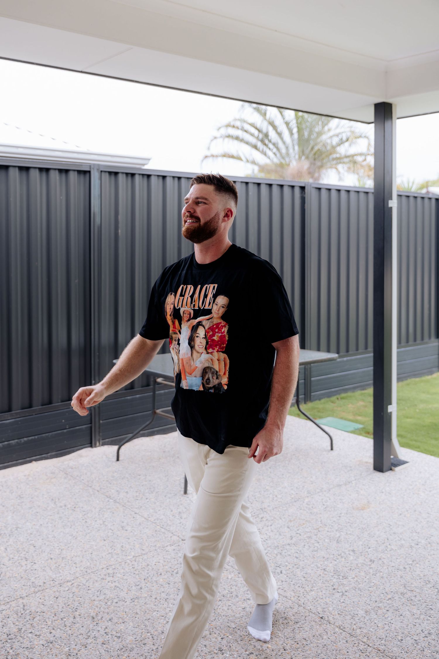 Person in black t-shirt and light pants walking along a modern covered patio with gravel floor and dark fence.