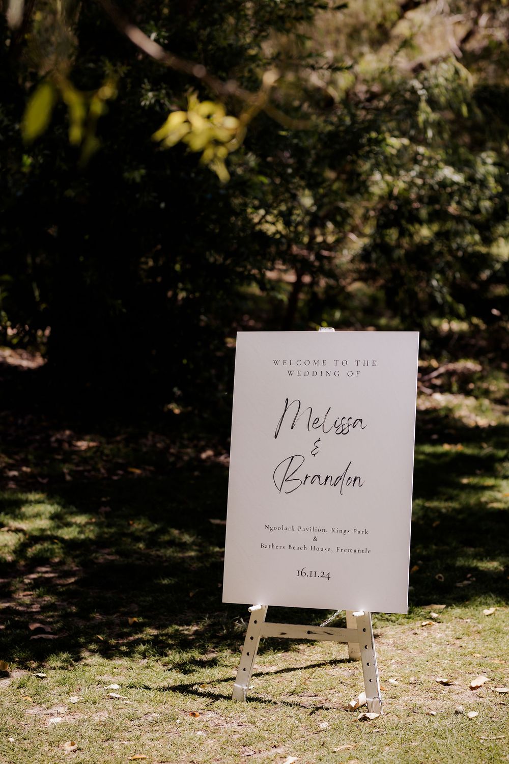 A series of white wedding signs displayed outdoors on stakes with natural foliage in the background.