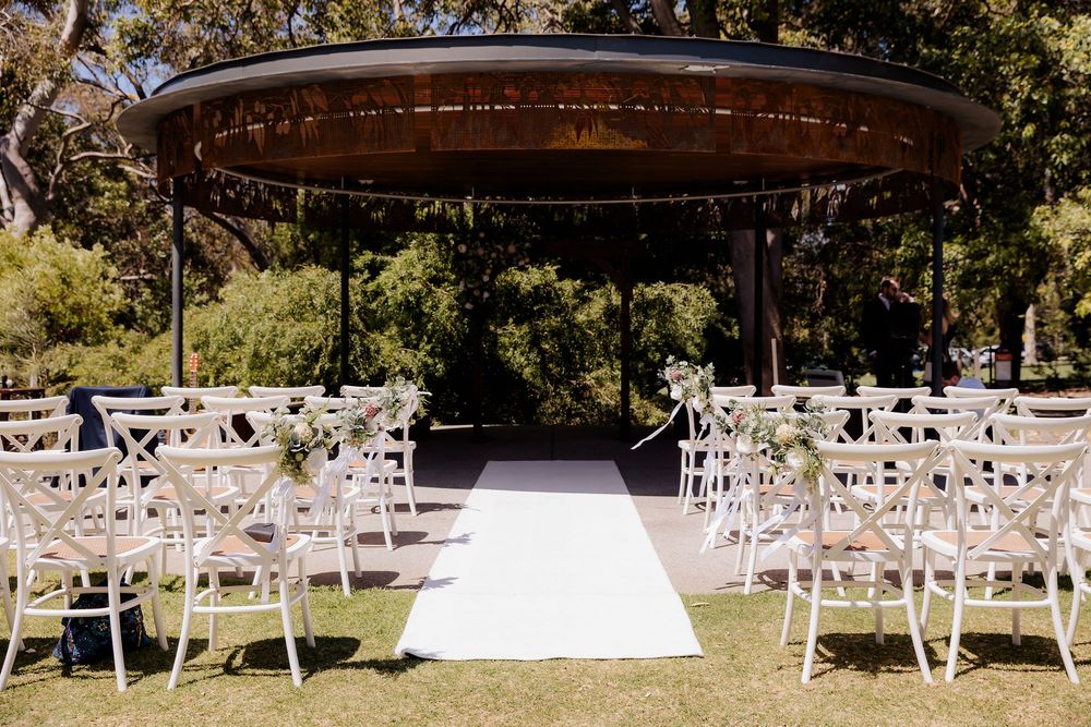 Elegant outdoor wedding ceremony setup with white chairs and gazebo under natural sunlight in garden setting.