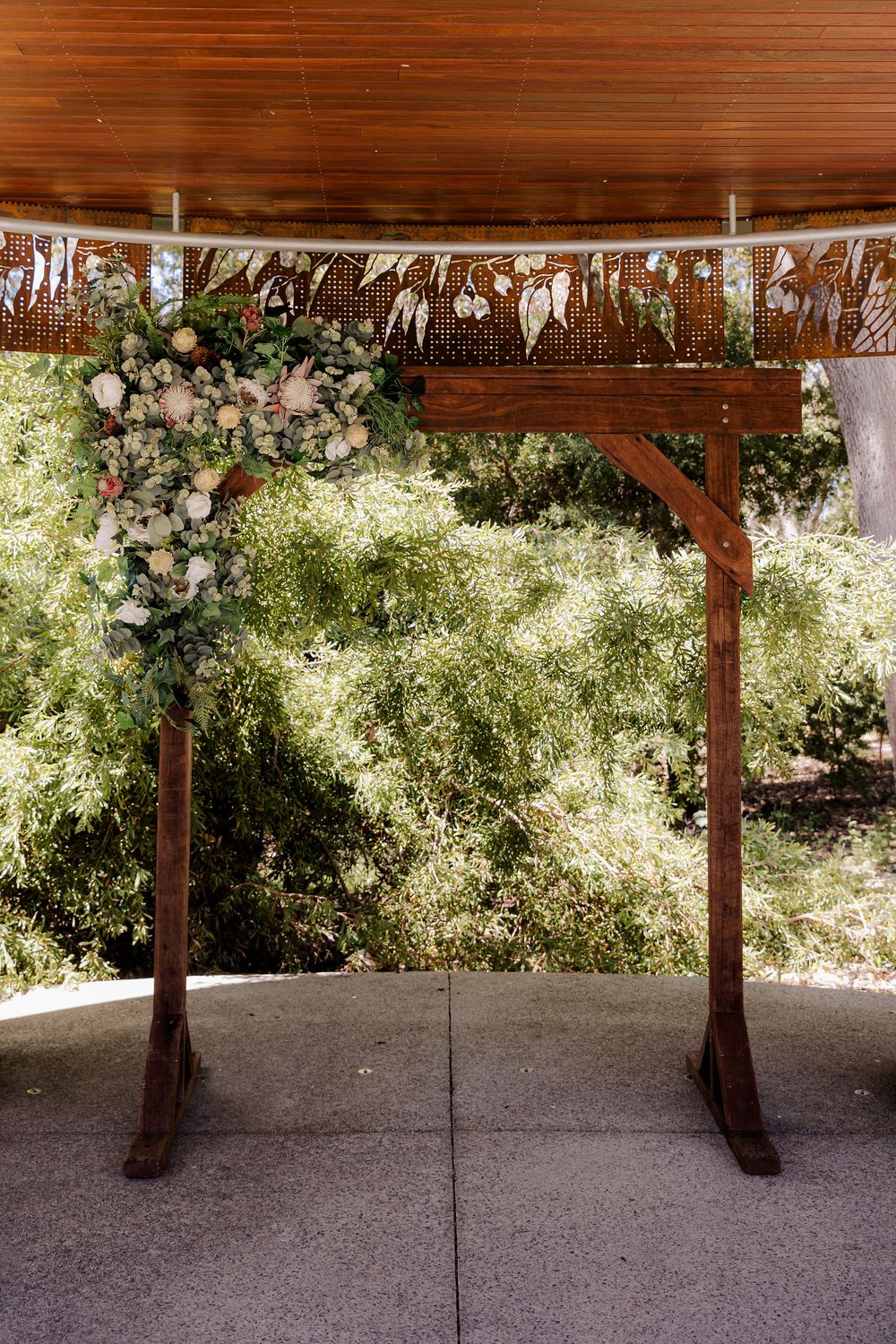 Wooden wedding arch decorated with pink florals and metallic streamers under a covered outdoor venue.