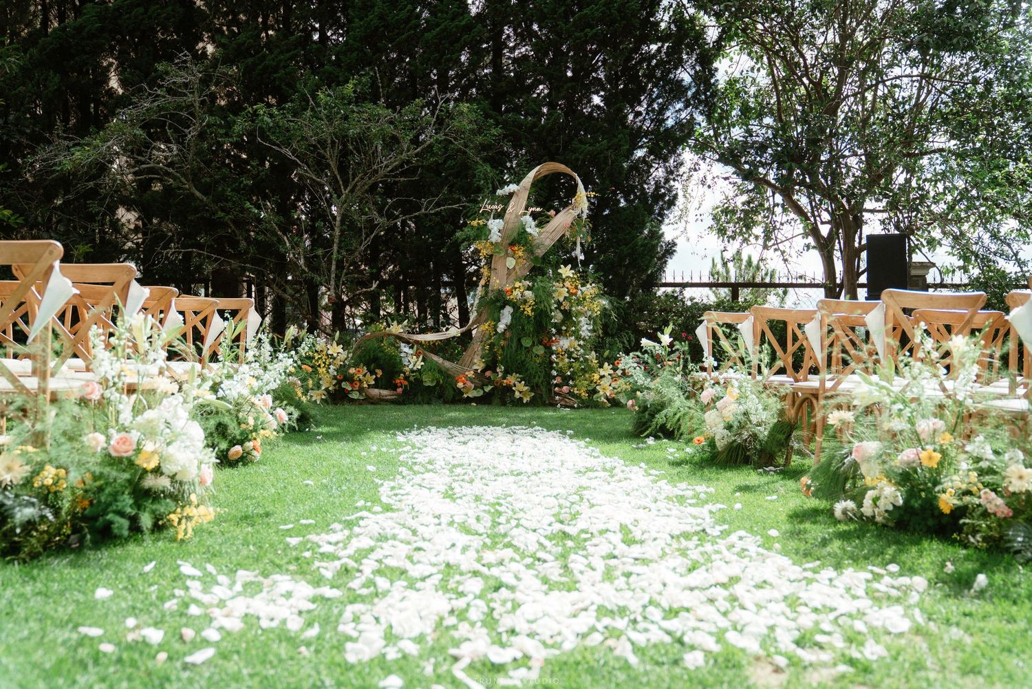 Elegant outdoor wedding ceremony aisle lined with lush floral arrangements and rose petal covered grass.