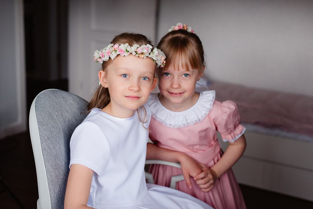 Portret dziewczynki z siostrą w wianku z białych kwiatów, uśmiechniętej, w miękkim świetle, w tle pokój