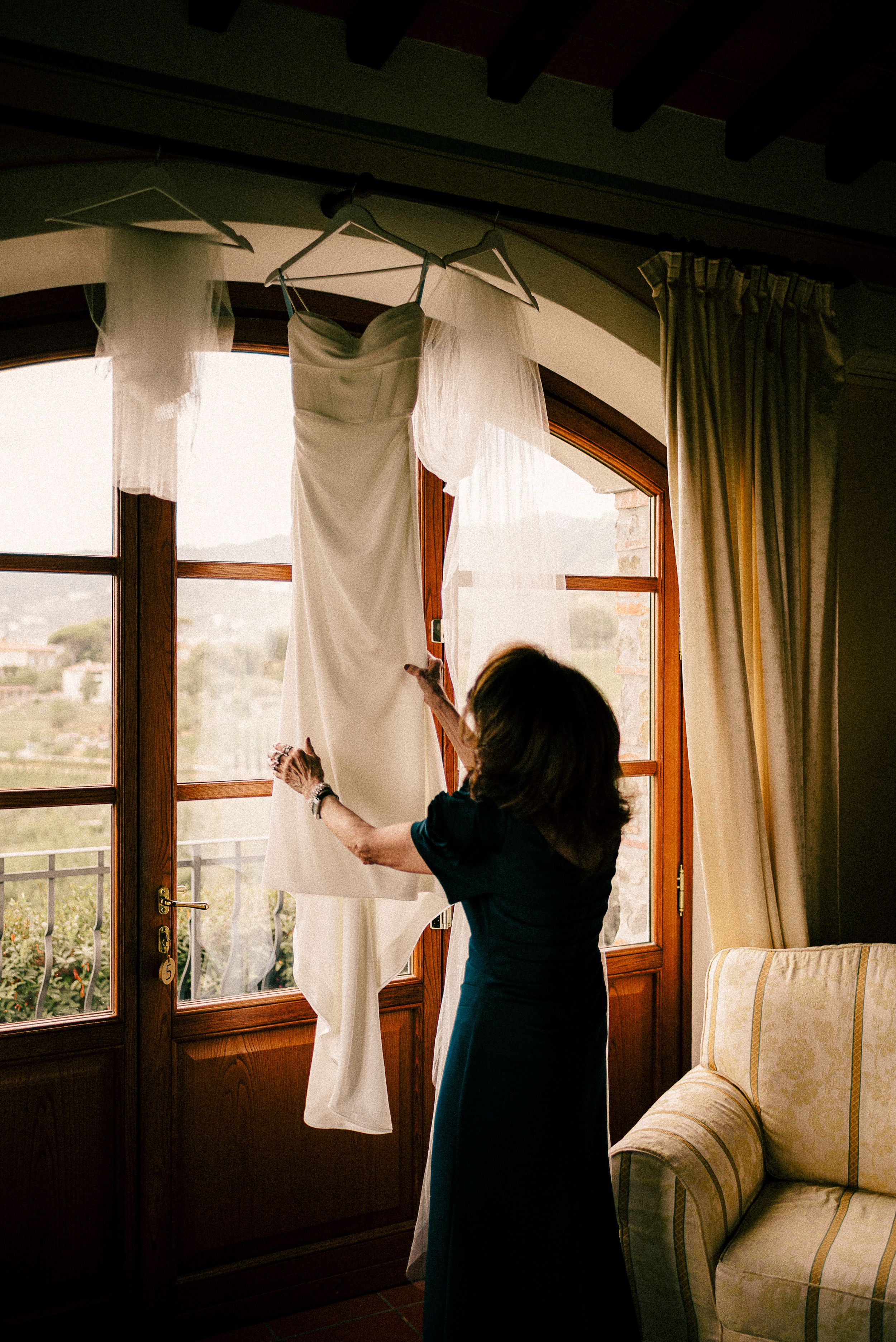 Silhouette hanging white clothes on a line by a window in moody lighting.