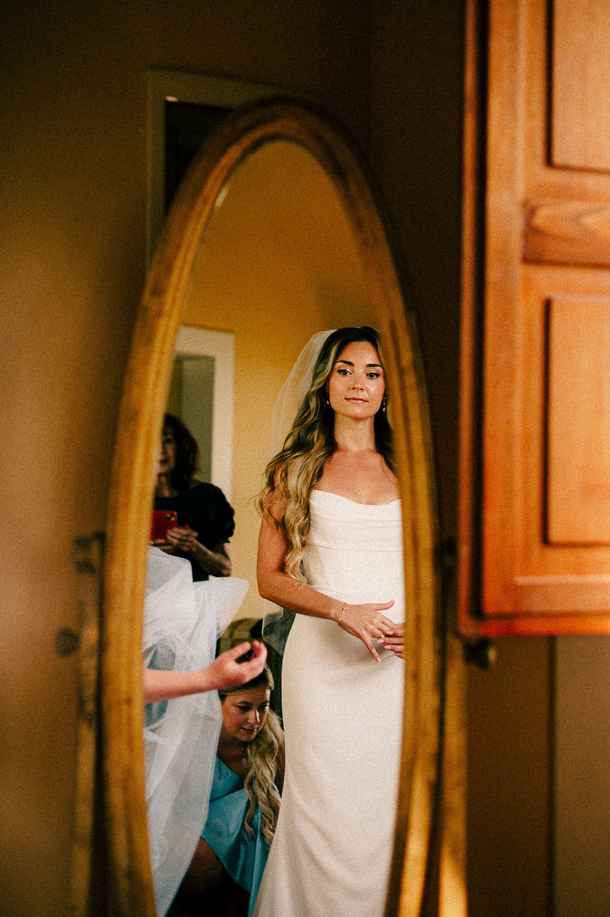 Getting ready scene with white dress reflections in an arched mirror.