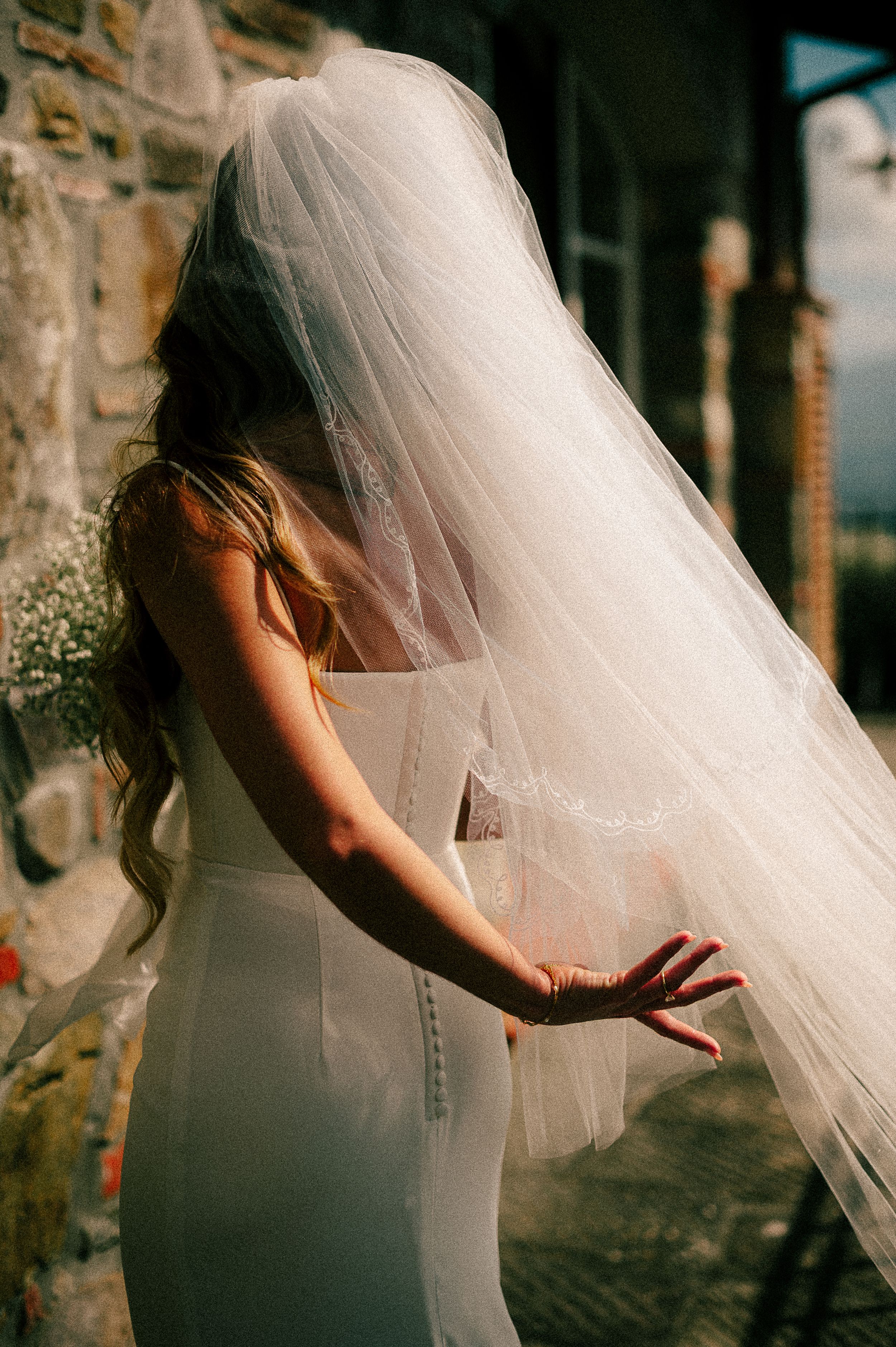 Artistic wedding photo capturing flowing veil movement against stone wall backdrop.
