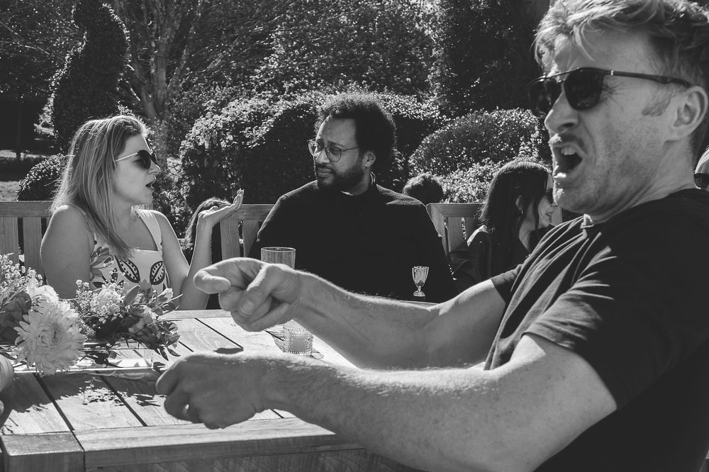 Group of wedding guests laugh and celebrate together on a sunny outdoor patio.