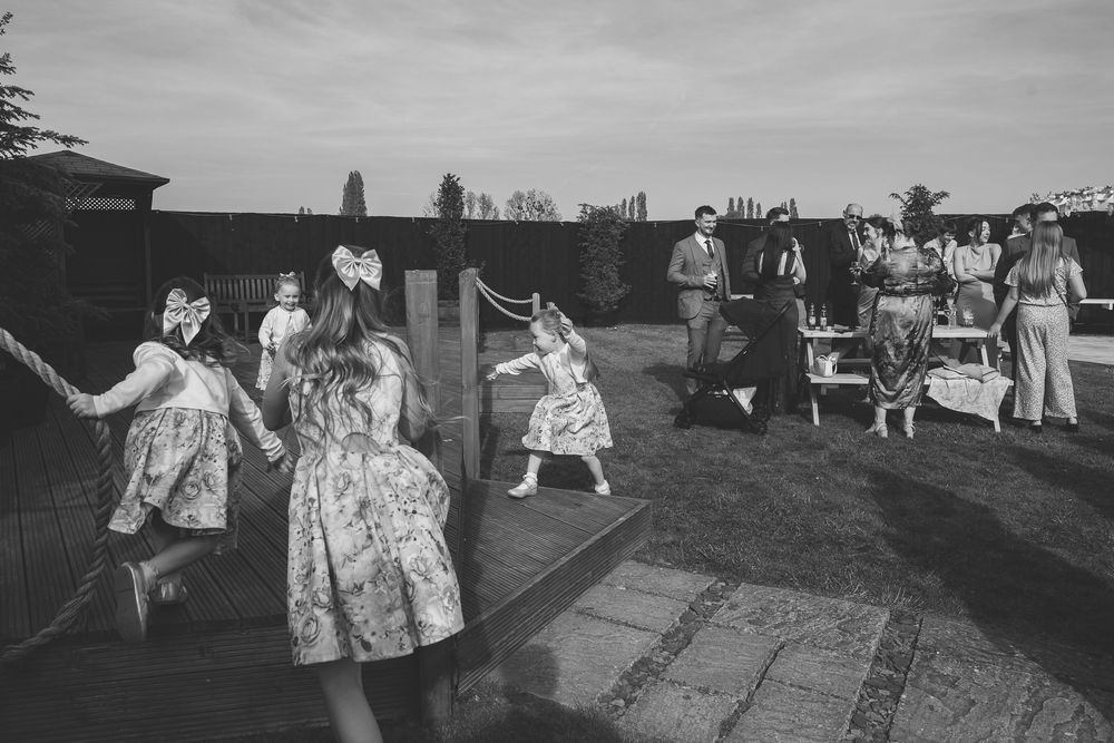 Black and white image of children playing at a suffolk wedding whilst adult guests socialise in the background.