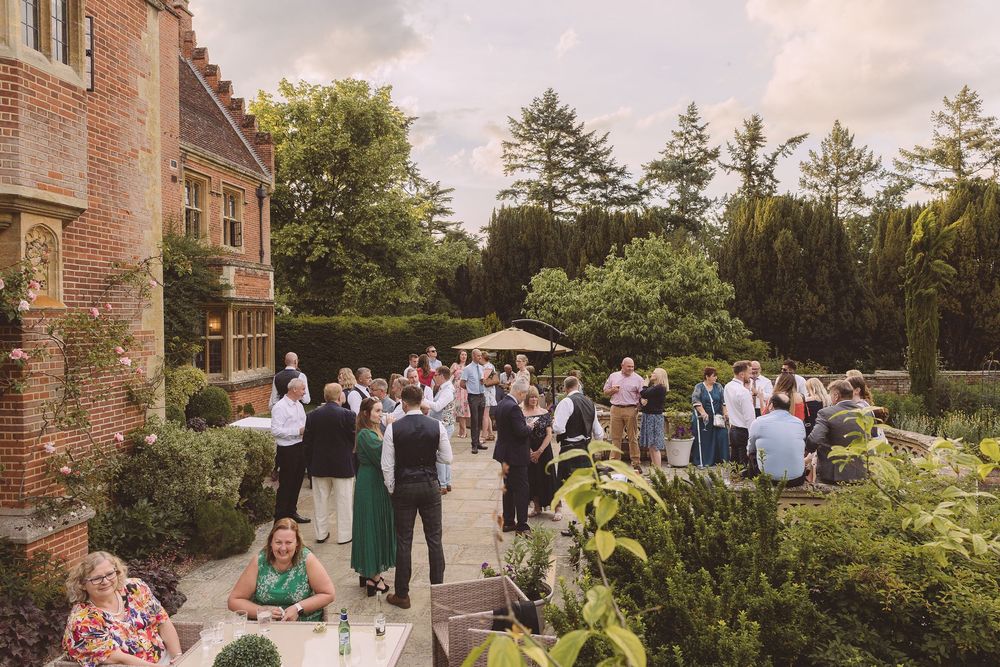 Wedding guests mingle in a garden courtyard outside Lanwades Hall in Suffolk during an evening reception.