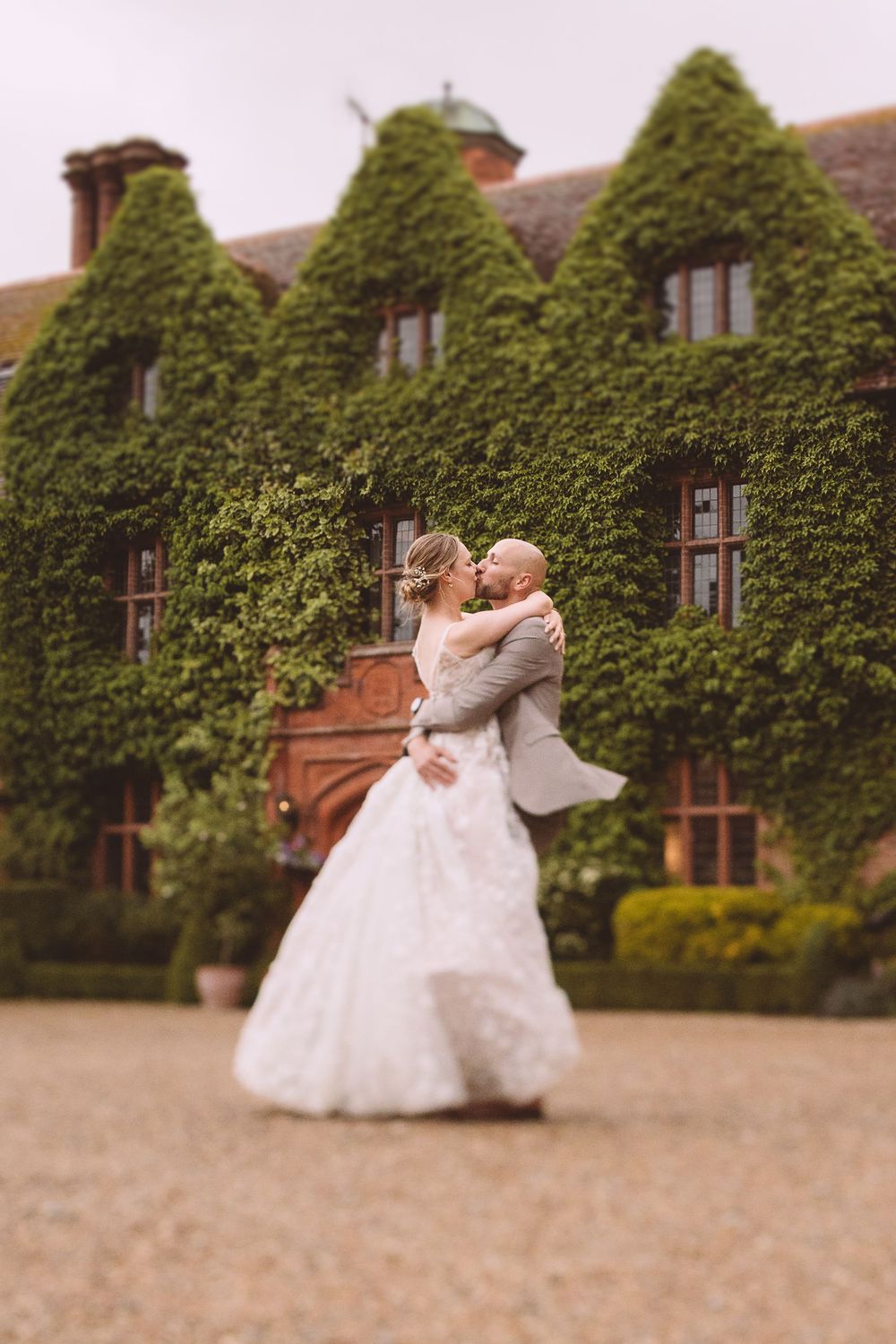 Wedding couple dances in front of ivy-covered Suffolk mansion Woodhall Manor.