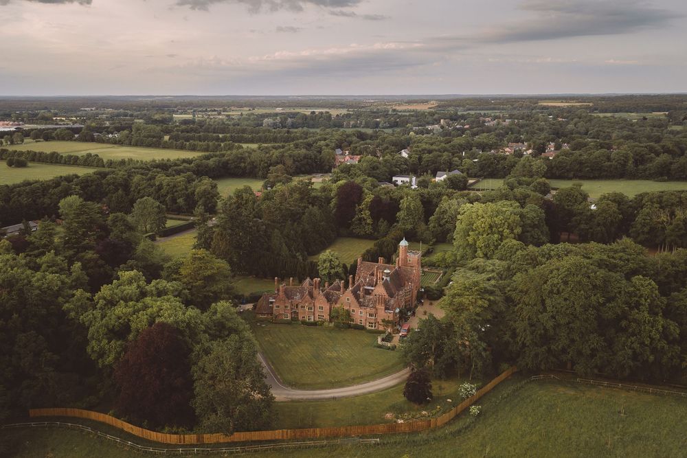 Aerial view of Suffolk Wedding venue Lanwades Hall surrounded by lush green gardens and wooded countryside on a cloudy day.