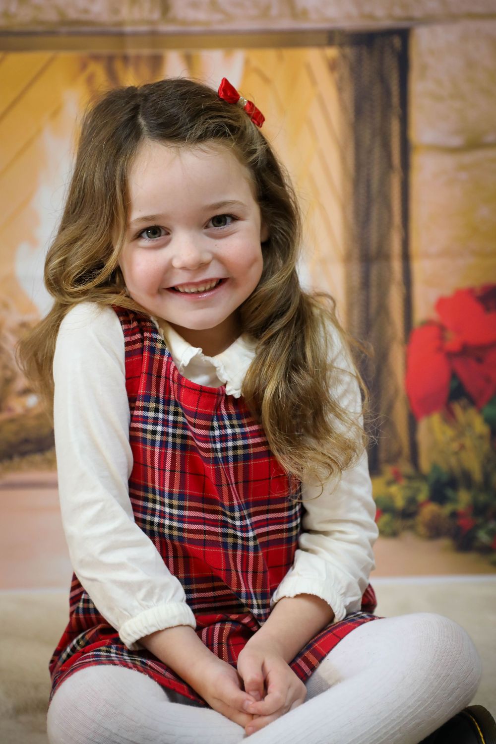 A series of holiday portraits showing a young child in a festive red plaid dress and white sleeves sitting against a warm backdrop.