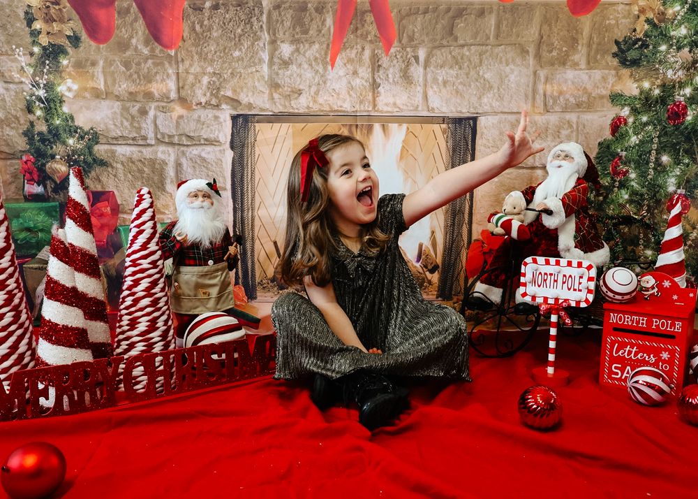 Festive Christmas photo backdrop with stone wall, red decor, candy canes, and holiday ornaments against red carpet.